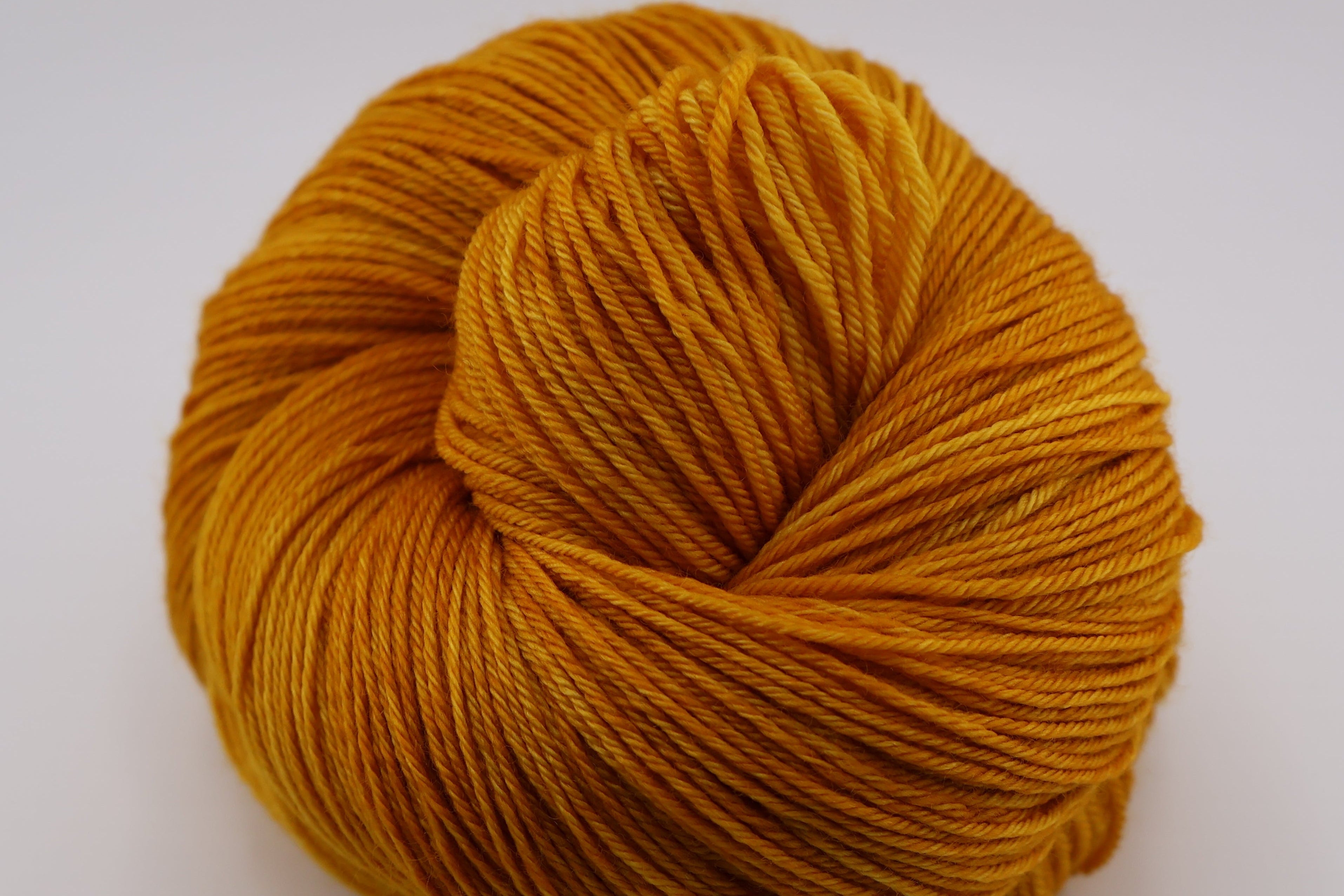 Ball of mustard yellow yarn on a white background