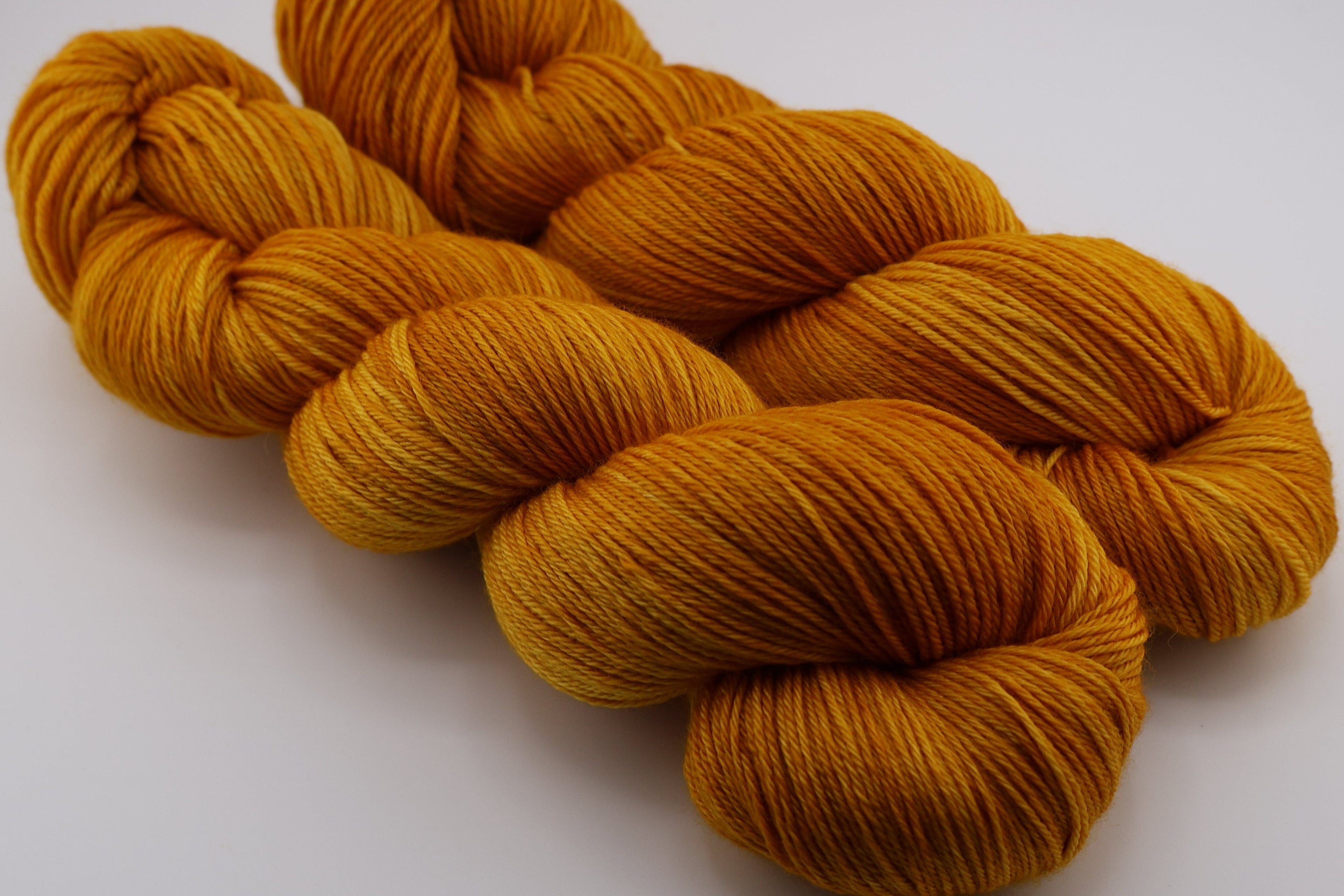 Two skeins of mustard yellow yarn on a white background